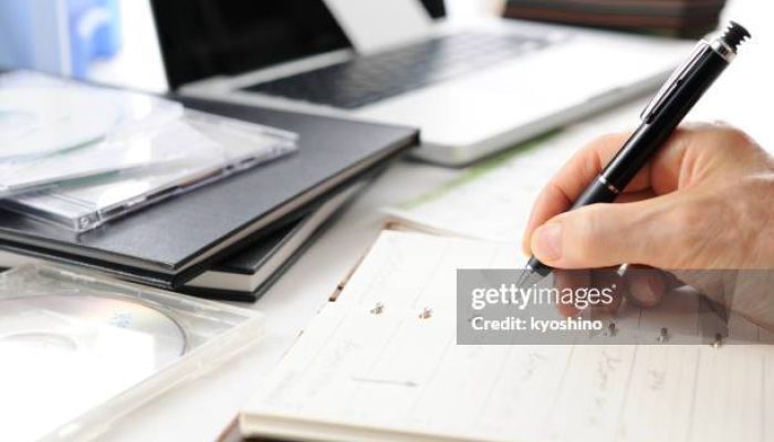 Close-up shot of hands with a pen and personal organizer on desk.